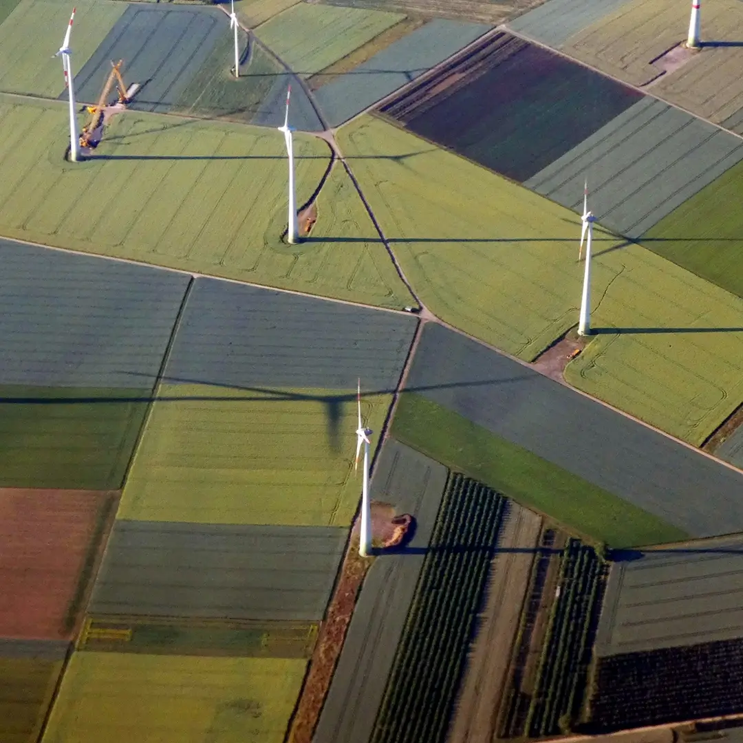 Mehrere Windräder stehen still auf weitläufigen Feldern, aufgenommen aus der Vogelperspektive – eine Verbindung von nachhaltiger Energie und Natur.