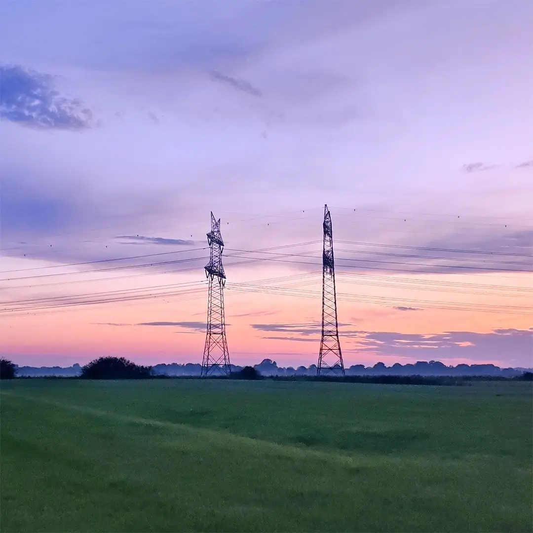 Hochspannungsmasten über einer Landschaft bei Sonnenuntergang