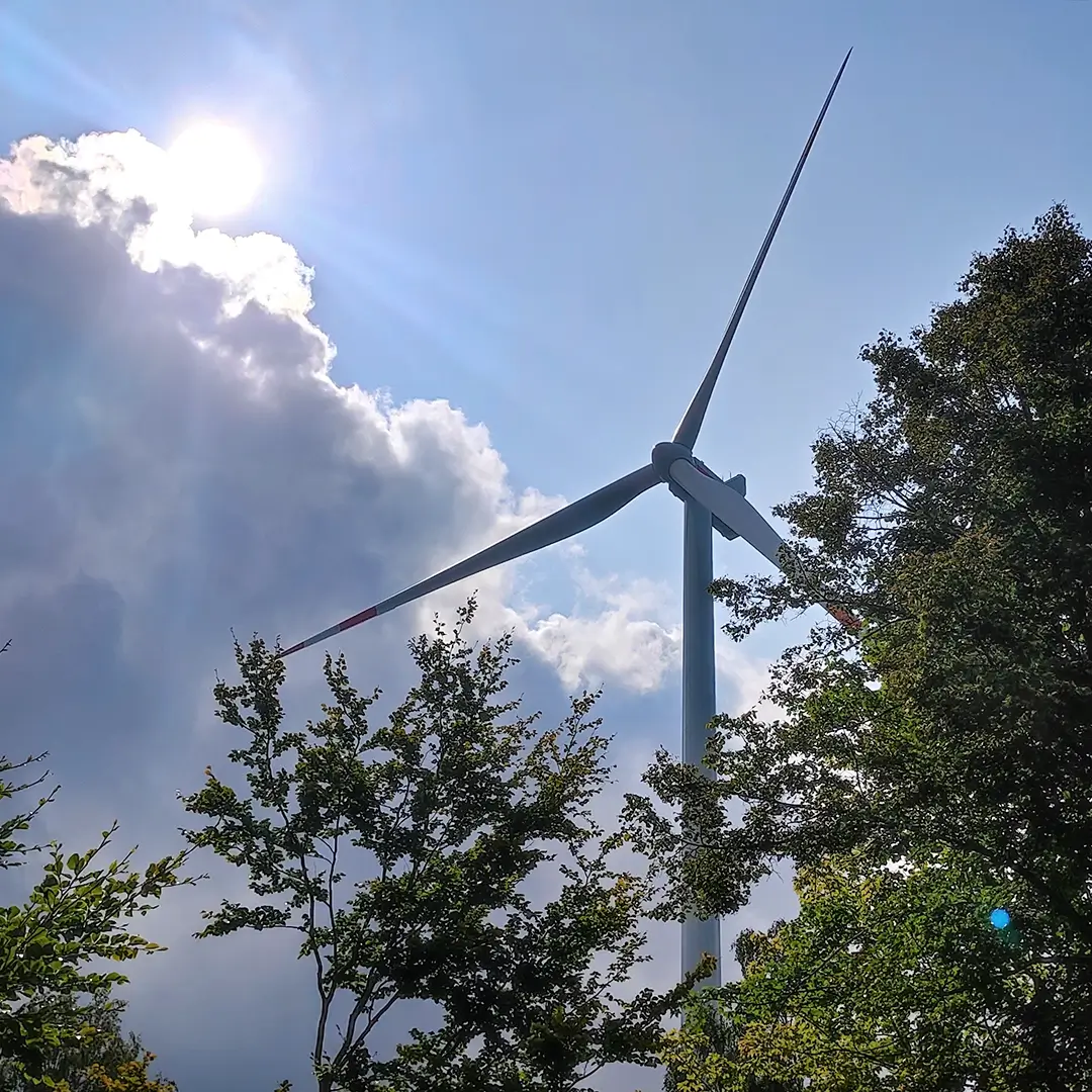 Windenergieanlage zwischen Bäumen bei Sonne und Wolken